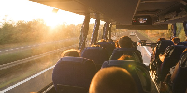 Background. Travel by bus. Bus interior. Salon of the bus with people fill the sun with light in the sunset. People travel on a big tourist bus. The bus rides along the mornings in the sunrise