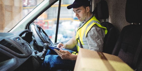 Delivery driver using tablet in van with parcels on seat